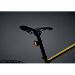 A bicycle seat with a black saddle and a yellow frame, featuring a small orange light attached below.