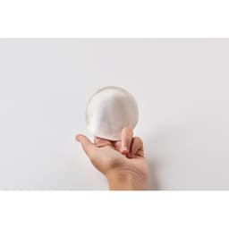 A hand holding a round, white cotton pad against a plain background.