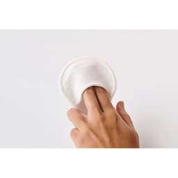 A white, round cotton pad held between fingers, suitable for application or removal of products.