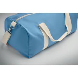 A blue duffle bag with cream-coloured handles and a zip closure. It features a branding logo.