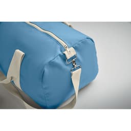 A blue duffel bag with a zip closure and a cream-coloured shoulder strap. The bag has a logo on the side.