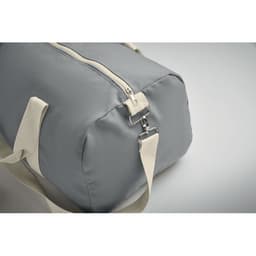 A grey duffel bag with a zip closure and cream straps. It has a metal clip attachment on the strap.