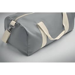 A grey duffel bag with cream handles and a zipper closure, featuring a small tag and a sleek design.