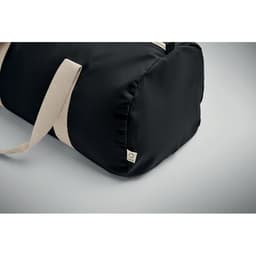 A black duffle bag with cream-coloured straps features a small logo tag. The bag has a rounded base.