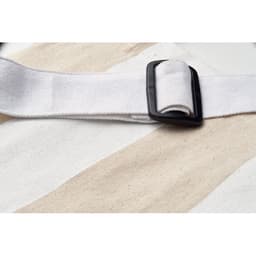 A close-up of a white strap with a black buckle on a patterned surface featuring light beige stripes.