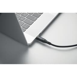 A close-up of a laptop with a black cable connected to one of its ports. The laptop features a silver finish.