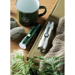 A set of two torches, one green and one silver, placed beside a green mug and stones on a wooden surface.