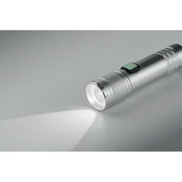 A silver torch with a textured grip and a green button, emitting a bright beam of light.
