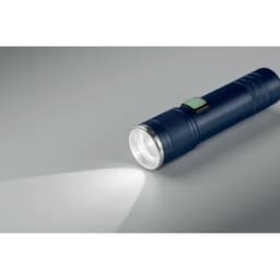 A blue flashlight is positioned on a grey surface, showcasing its shiny silver light beam and textured grip.