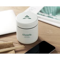 A white container with a green lid and branding, placed on a wooden surface with chopsticks and a phone nearby.