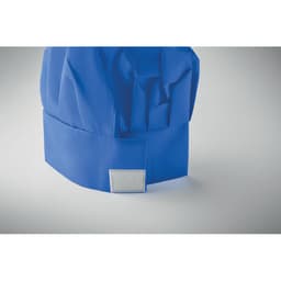 A blue chef's hat with a folded brim and a grey patch on the side, laid against a neutral background.