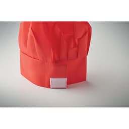 A red chef hat made of fabric featuring a plain white patch on the front.