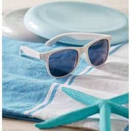 A pair of white sunglasses with blue lenses rests on a blue and white striped towel, next to a frisbee and a starfish.