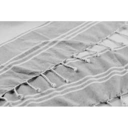 A grey towel with white stripes and tassels along the edges, featuring a textured fabric.