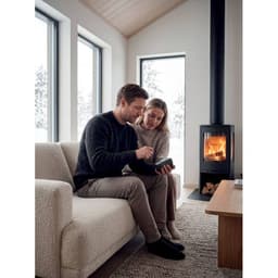 A couple sits close together on a light-coloured sofa, with a fireplace glowing in the background.