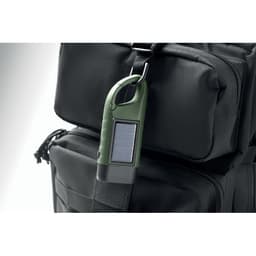 A green solar-powered device attached to a black backpack, featuring a carabiner and a small screen.