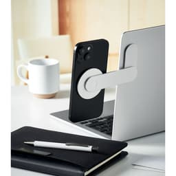 A smartphone with a white grip is positioned against a laptop, alongside a coffee mug and a notebook on a desk.
