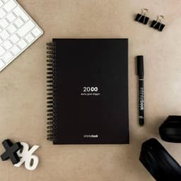 An A5 infinite diary in black, accompanied by a black marker, binder clips, and headphones on a beige surface.