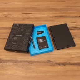 A hard-covered black Infinitebook A5 planner, blue cleaning kit, marker, and ballpoint holder arranged on a wooden surface.
