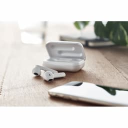 A pair of white wireless earbuds with a charging case on a wooden surface, alongside a smartphone.