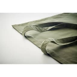 A green tote bag with long handles rests on a neutral surface, showcasing its fabric texture and design.