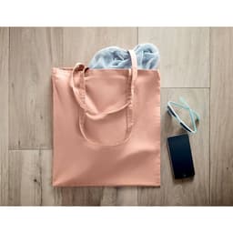 A peach-coloured tote bag with a pair of grey shoes, glasses, and a smartphone beside it on wooden flooring.