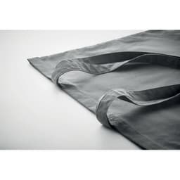 A grey cloth bag with long handles laid flat on a surface, featuring a simple and minimalist design.