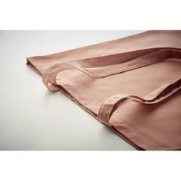 A folded soft pink fabric with smooth edges and straps, lying flat on a white surface.
