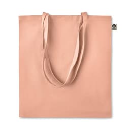 A tote bag in a soft peach colour with long handles and a simple design. It features a small logo tag.