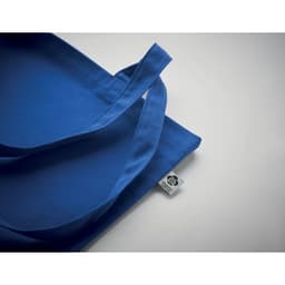 A blue tote bag with long handles and a small tag on the side.