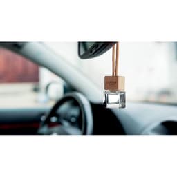 A wooden car air freshener hangs from the rear-view mirror, featuring a clear glass container filled with fragrance.