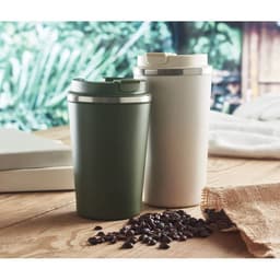Two drink bottles in green and white, with silver lids, placed beside coffee beans on a wooden surface.