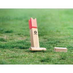 A wooden lawn game piece with a pink crown-shaped top, featuring a logo, resting on grass.