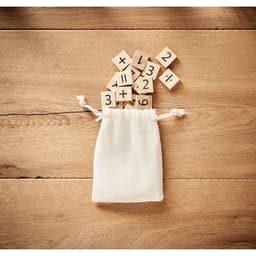 A beige drawstring pouch with wooden number tiles scattered around it on a wooden surface.