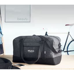 A grey duffel bag with a shoulder strap and branding, sitting on a table beside a bicycle.