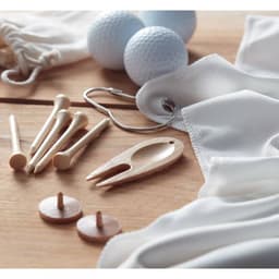 A wooden tee tool, golf tees, and blue golf balls on a wooden surface, alongside a white fabric pouch and keyring.