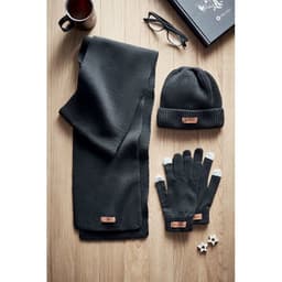 A grey knit scarf, beanie, and gloves laid out on a wooden surface, alongside a mug, glasses, and a book.