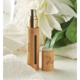A drink bottle in a bamboo casing with a gold spray nozzle and a removable lid, surrounded by white flowers and green leaves.