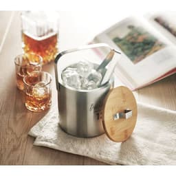 A drink bottle in a stainless steel ice bucket, featuring a bamboo lid, with glasses and a book nearby.