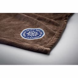 A brown fleece blanket featuring a circular logo in blue and white at one corner.
