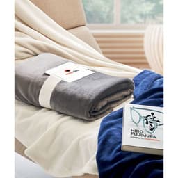 A soft grey blanket neatly rolled with a tag, placed on a beige chair alongside a book and a navy blue item.