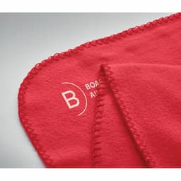 A red fleece blanket with a stitched edge and a logo on one corner.
