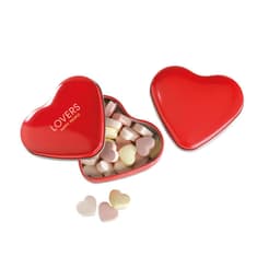 A heart-shaped red tin filled with pastel-coloured heart-shaped sweets, with some sweets scattered nearby.