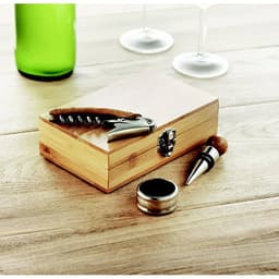 A wooden gift box containing a corkscrew, wine stopper, and a foil cutter, with a green bottle and glasses nearby.