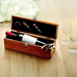 A wooden box containing a wine bottle, corkscrew, and wine accessories, beside two glass cups on a wooden surface.