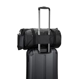 A cylindrical black sports bag made of high-density recycled polyester sits atop a suitcase, featuring a side compartment for shoes.