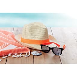 A straw hat with an orange band, black sunglasses, and a coral beach towel displayed on a wooden surface.