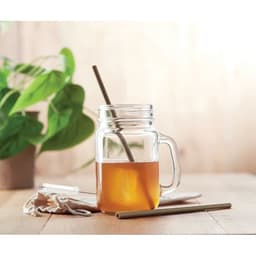 A drink bottle with a natural straw, featuring a glass jar filled with a brown beverage on a wooden surface with greenery.