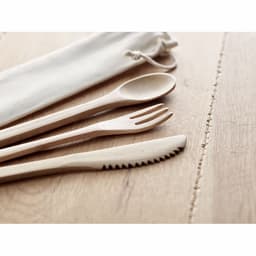 A set of wooden cutlery including a spoon, fork, and knife, displayed on a wooden surface with a fabric pouch.