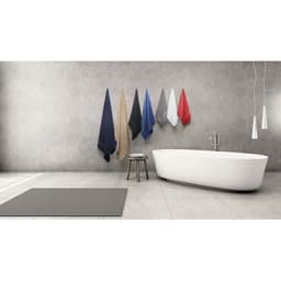 A selection of towels in various colours hanging on a wall beside a modern bathtub and a small stool in a bathroom setting.